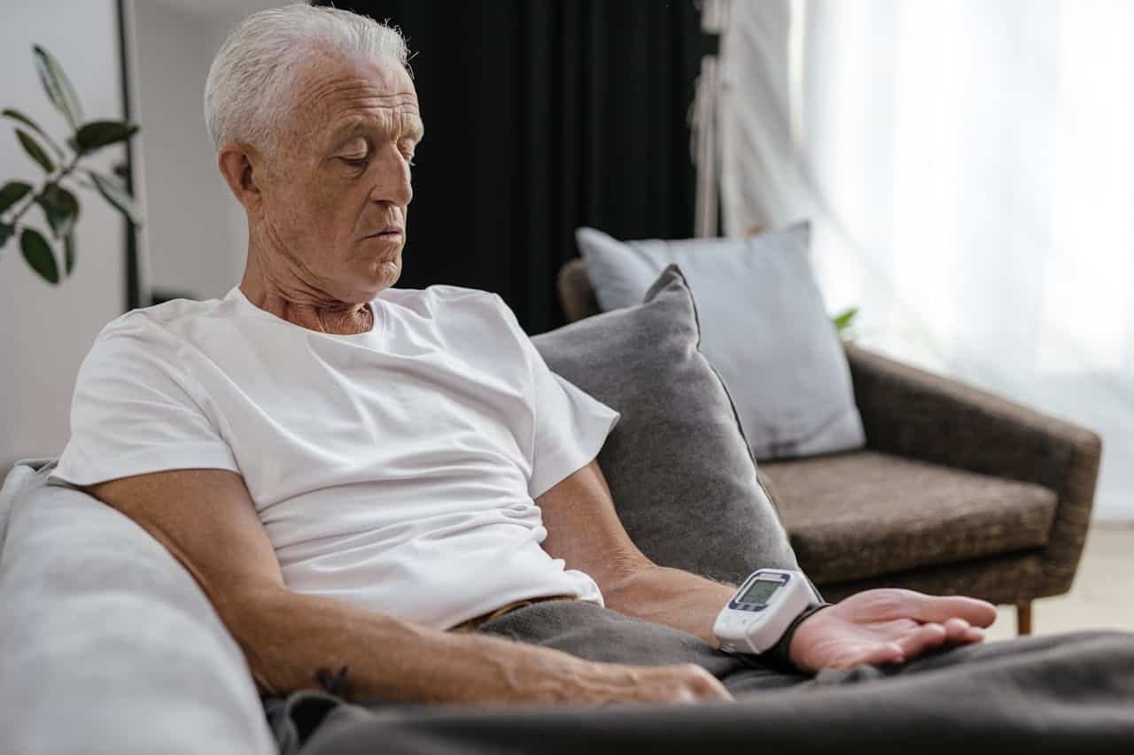 Elderly man measuring blood pressure with digital device while relaxing at home.